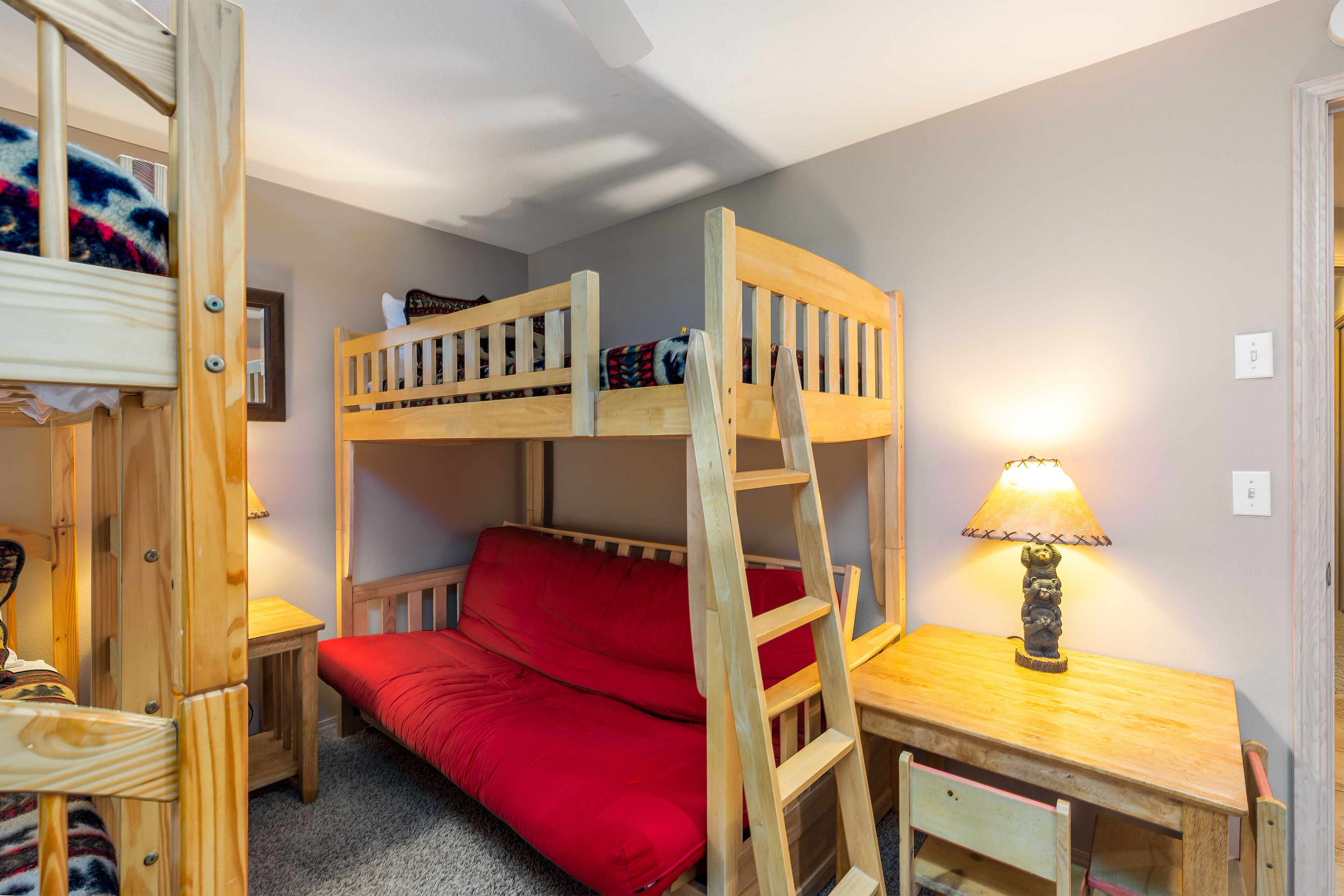 Une chambre avec un lit superposé, un matelas rouge, un bureau en bois et une lampe.