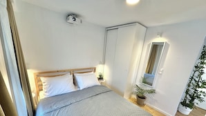 A bedroom with a bed, bedside table, lamp, potted plant, and a ceiling projector.