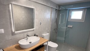 A modern bathroom with a wooden vanity, a large mirror, a white sink, a toilet, and a glass-enclosed shower.