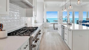 A modern kitchen with a large island, a gas stove, and a view of the ocean. - Viviana #12 | Luxury Gulf Front Home, Private Pool + Incredible Views! (Pensacola)