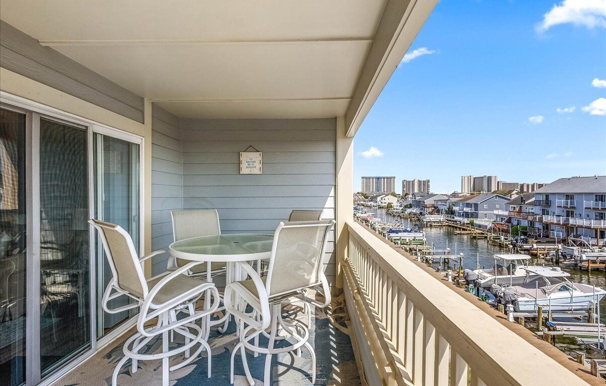 A balcony with a table and chairs, overlooking a marina with boats and buildings.