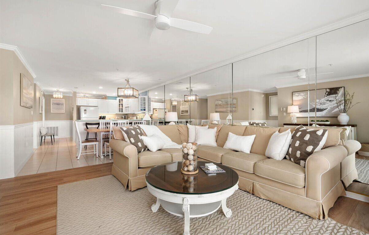 Een ruime woonkamer met een beige bank, een rond bijzettafeltje en een eethoek op de achtergrond.