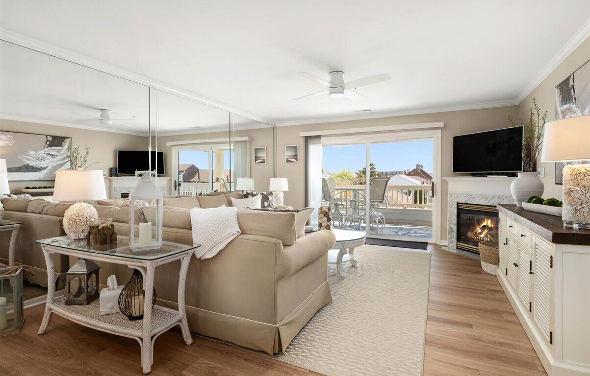 A spacious living room with a beige sofa, a glass coffee table, and a fireplace.