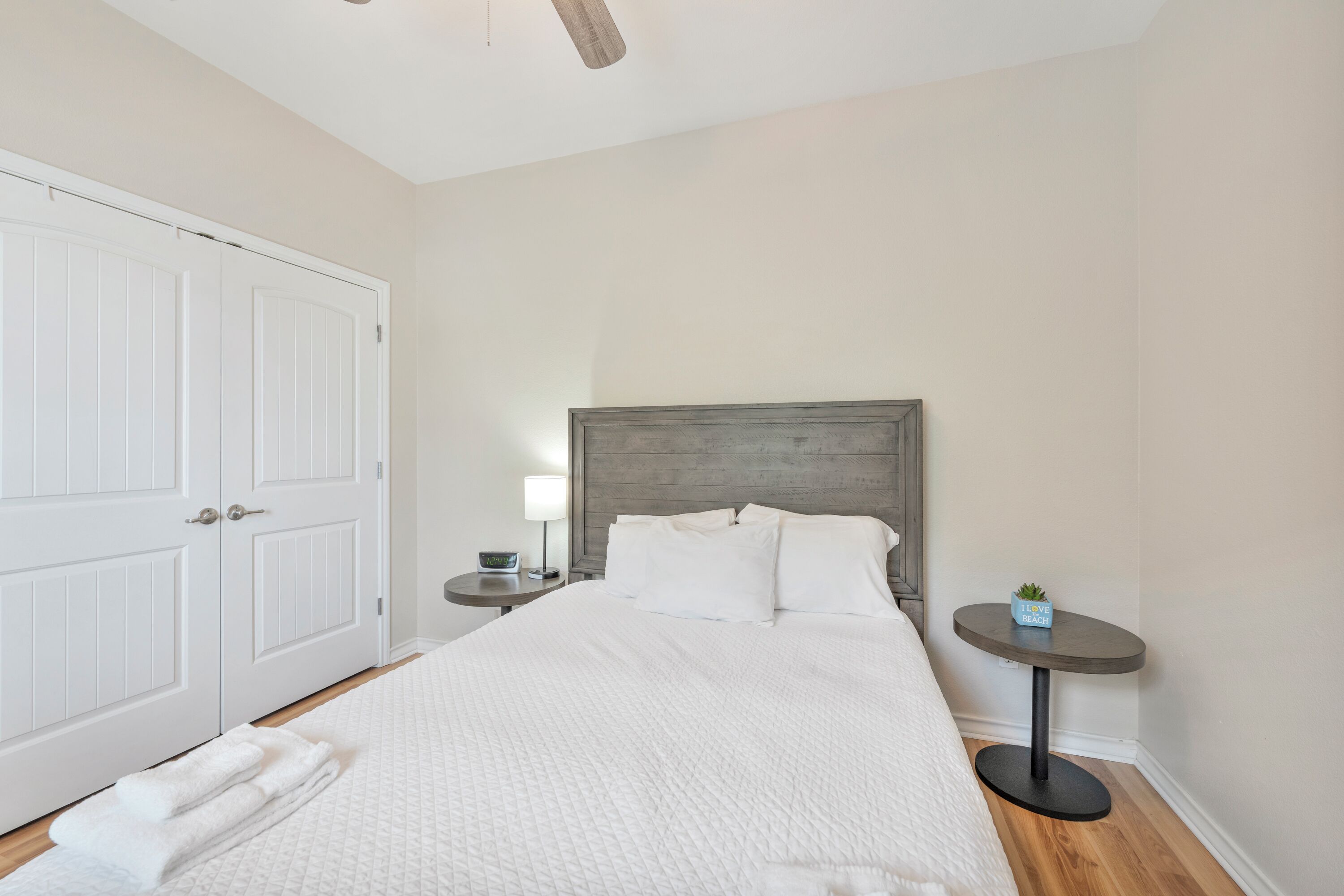 A bedroom with a large bed, a wooden headboard, a bedside table with a lamp, and a small plant.