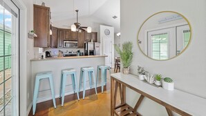 A kitchen with wooden cabinets, a central island with stools, a round mirror, and potted plants.