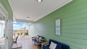 A covered patio area with a green wall, a blue sofa, two wooden chairs, and a small table.