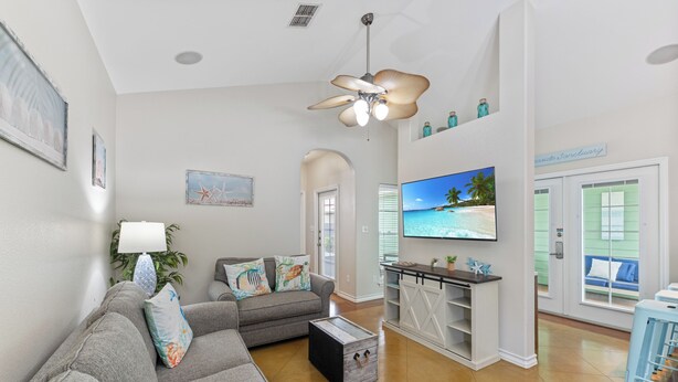 A living room with a grey sofa, a coffee table, a TV, and a ceiling fan.