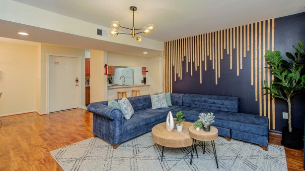 Una sala de estar moderna con un sofá seccional azul, dos mesitas de madera redondas, una alfombra estampada, un colgador de luz y un panel de madera vertical en la pared.