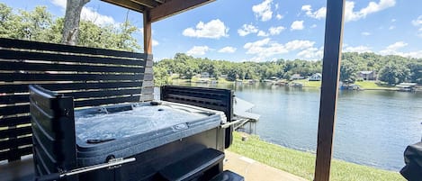 A hot tub under a wooden pergola with a view of a lake and houses in the background.