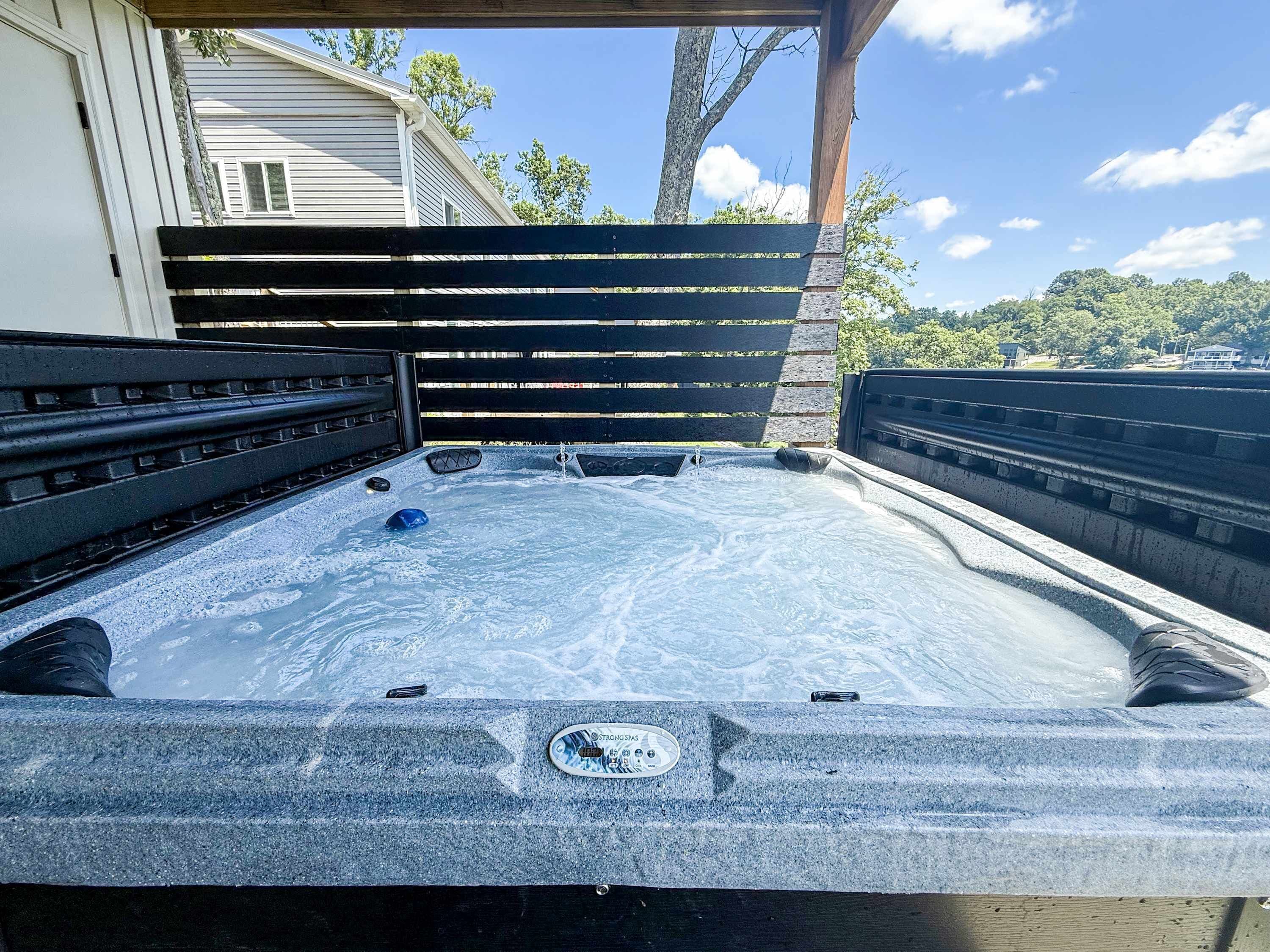 Un bain à remous avec une terrasse en bois et une vue sur une maison et des arbres.