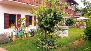 A two-story building with balconies, a garden with various plants and flowers, and outdoor seating. - Spazioso Appartamento Alle Porte Delle Dolomiti (Arten)