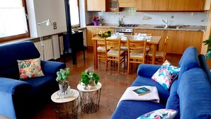 A living room with a sofa, two small side tables with plants, and a dining area with a table and chairs. - Spazioso Appartamento Alle Porte Delle Dolomiti (Arten)