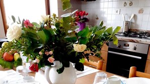 A dining table set with white plates, bowls, and cutlery, a vase with flowers, and a kitchen in the background. - Spazioso Appartamento Alle Porte Delle Dolomiti (Arten)
