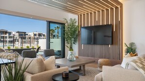 A modern living room with a large TV, comfortable seating, a coffee table, and a view of the cityscape. - Modern Lagoon: Desert Color Lagoon + Beaches (St. George)