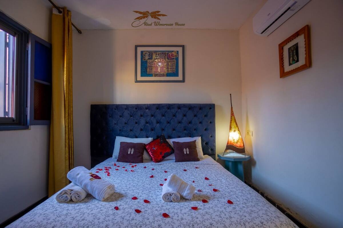 A neatly made bed with a floral bedspread, two pillows, and rolled towels.