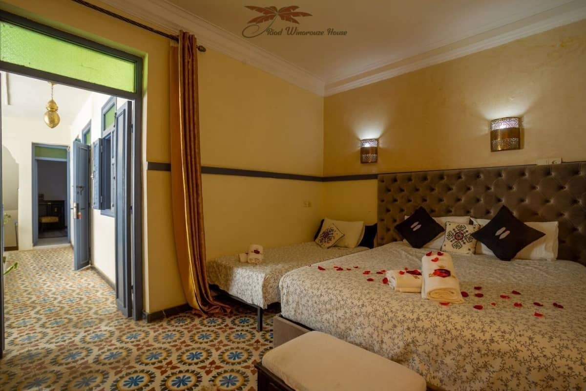 A hotel room with two beds, a large window, a patterned floor, and a green door.
