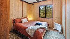 Quarto com painéis de madeira, cama, janela e radiador.