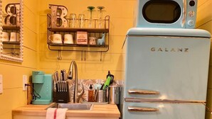 Une cuisine compacte avec un réfrigérateur Galanz bleu clair, un évier équipé de divers ustensiles et une étagère au-dessus de l’évier où sont rangés les accessoires de cuisine.