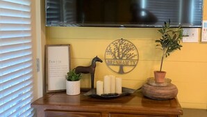 Un meuble en bois surmonté d’un téléviseur à écran plat, avec un tableau encadré, une plante en pot et une assiette décorative ornée d’un motif d’arbre.