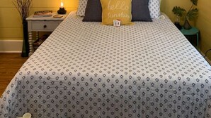 Une chambre à coucher avec une couvre-lit à motifs, une tête de lit décorative, une table de chevet avec une lampe et un tableau encadré accroché au mur.