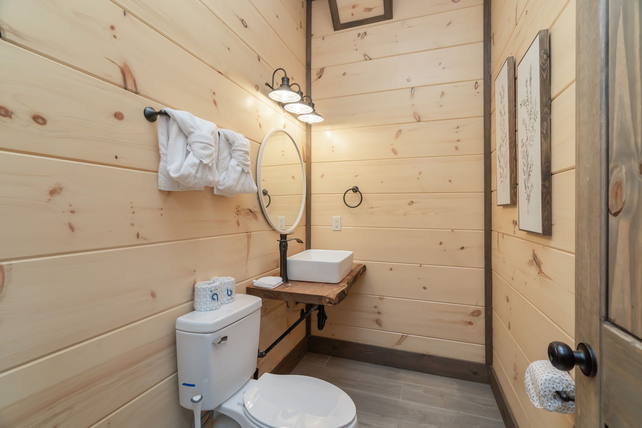 A compact wooden bathroom with a toilet, sink, and a mirror.