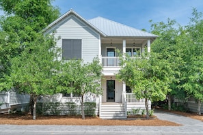 A two-story house with a front porch, a covered entryway, and a small front yard with trees and shrubs.