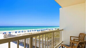 A balcony with a view of the beach, wooden chairs, and a wooden deck.