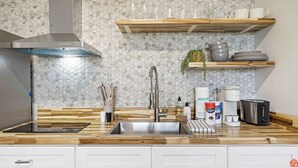 A modern kitchen with a stainless steel sink, wooden countertop, and a hexagonal tile backsplash.