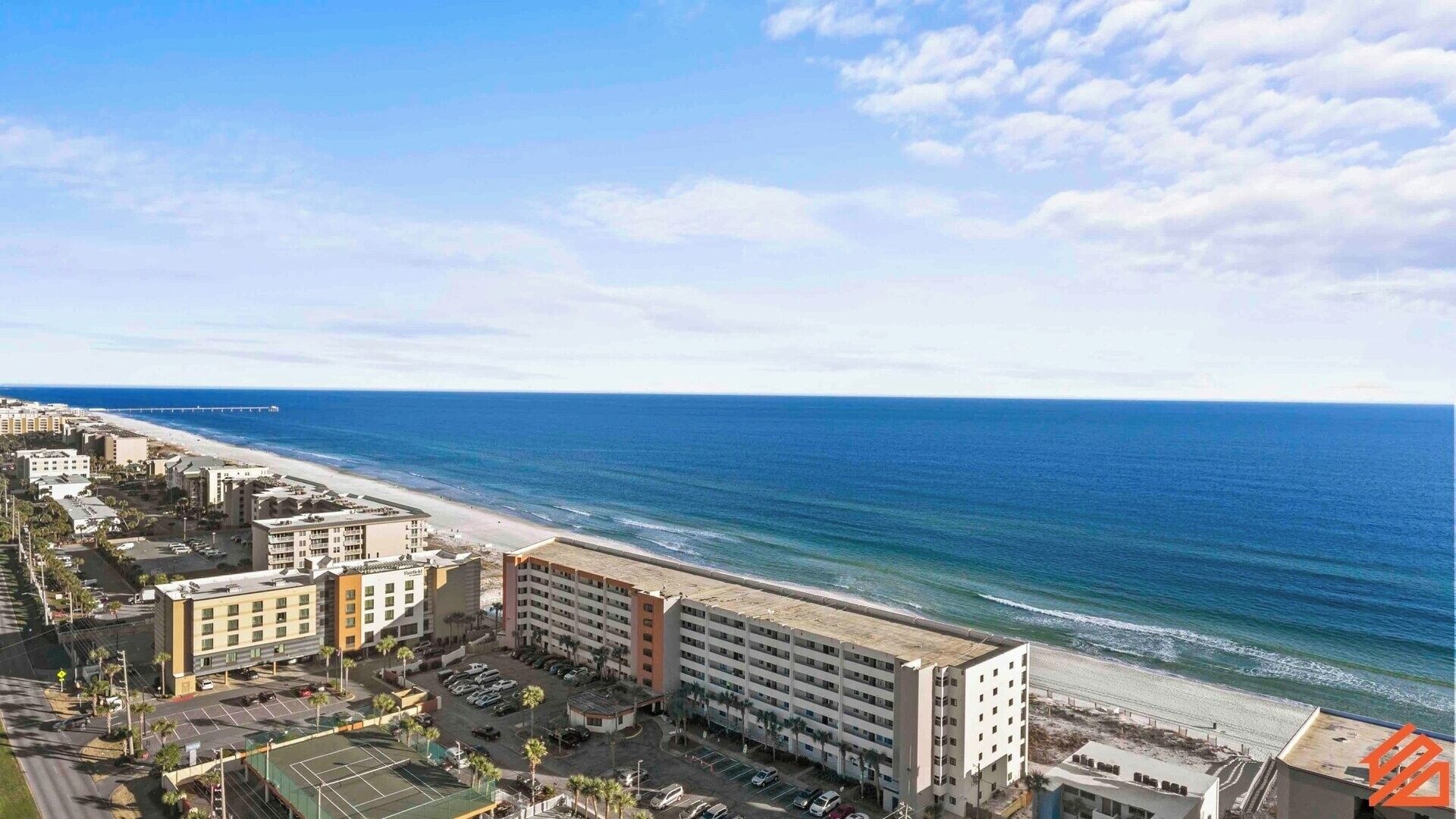 Un hotel costero con varias edificaciones, una playa y un muelle al fondo.