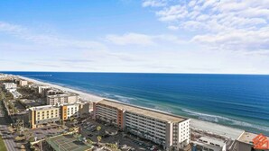 A coastal hotel with multiple buildings, a beach, and a pier in the background.