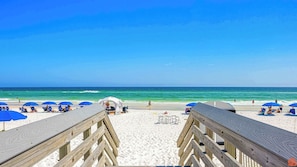 A beach with wooden walkways, blue umbrellas, and a clear view of the ocean.
