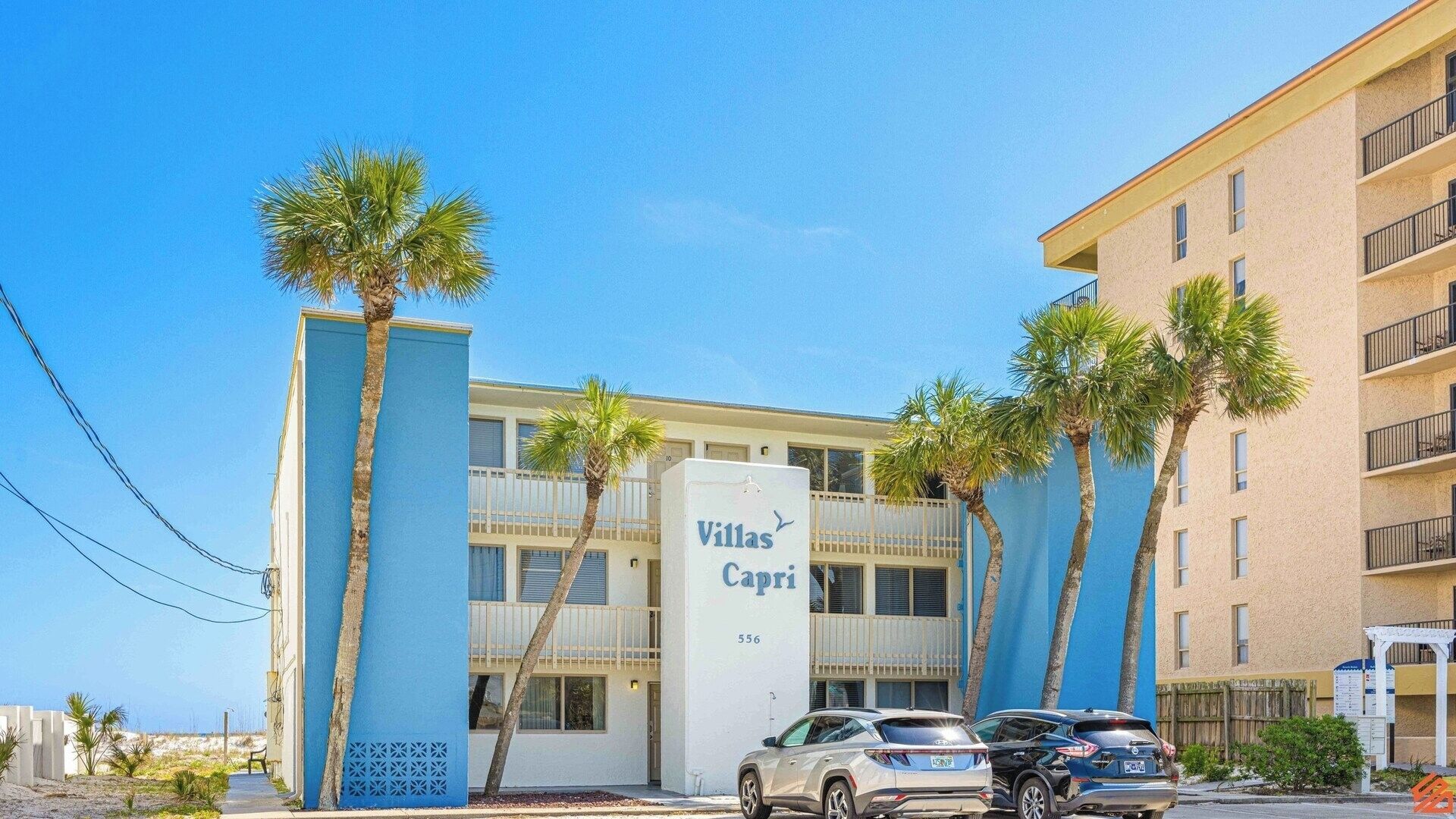 Un edificio con un letrero que dice "Villas Capri" y el número 556. Hay palmeras al frente y coches estacionados.