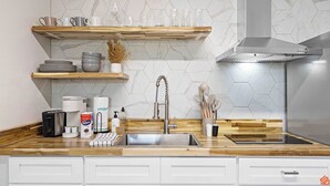 Una cocina moderna con un lavamanos de acero inoxidable, estantes de madera y un salpicadero de azulejos hexagonales.