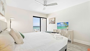 Habitación de hotel con una cama grande, ventilador de techo, televisor y balcón con vista a la playa.
