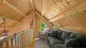 Quarto de sótão com vigas de madeira, um sofá, uma cadeira e um abajur.