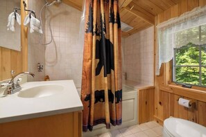 A bathroom with a wooden interior, a white sink, a shower curtain with a bear design, and a window with a view of greenery.