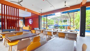 Un amplio comedor interior con varias mesas y sillas, ventanas grandes que ofrecen vistas a zonas verdes y ventiladores de techo.