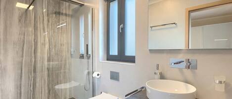 Une salle de bain moderne avec une douche à parois de verre, des toilettes blanches, un grand lavabo rond et un miroir au-dessus du lavabo.