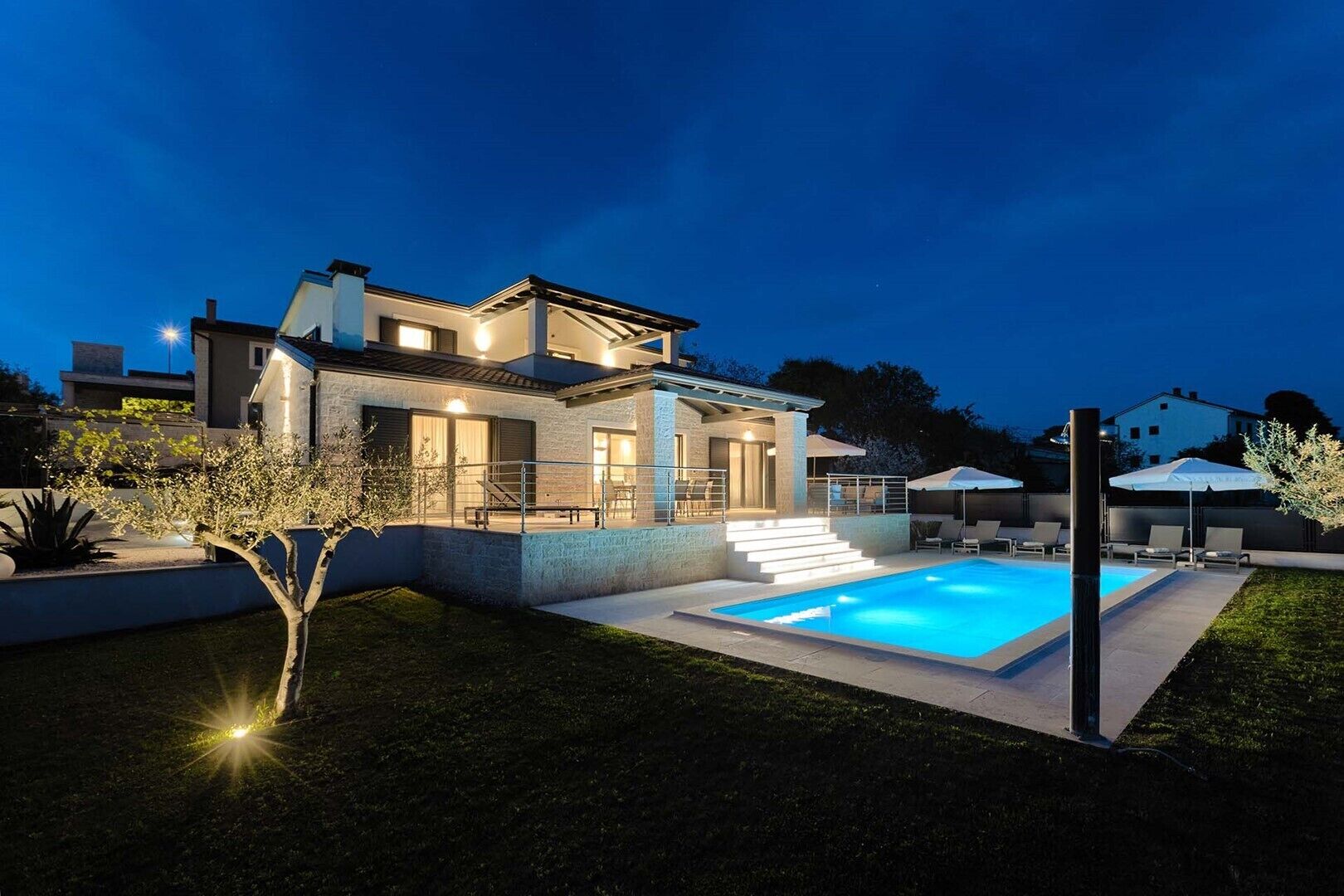 Ein modernes, zweistöckiges Haus mit Swimmingpool, Sitzgelegenheiten im Freien und einer gut beleuchteten Terrasse.