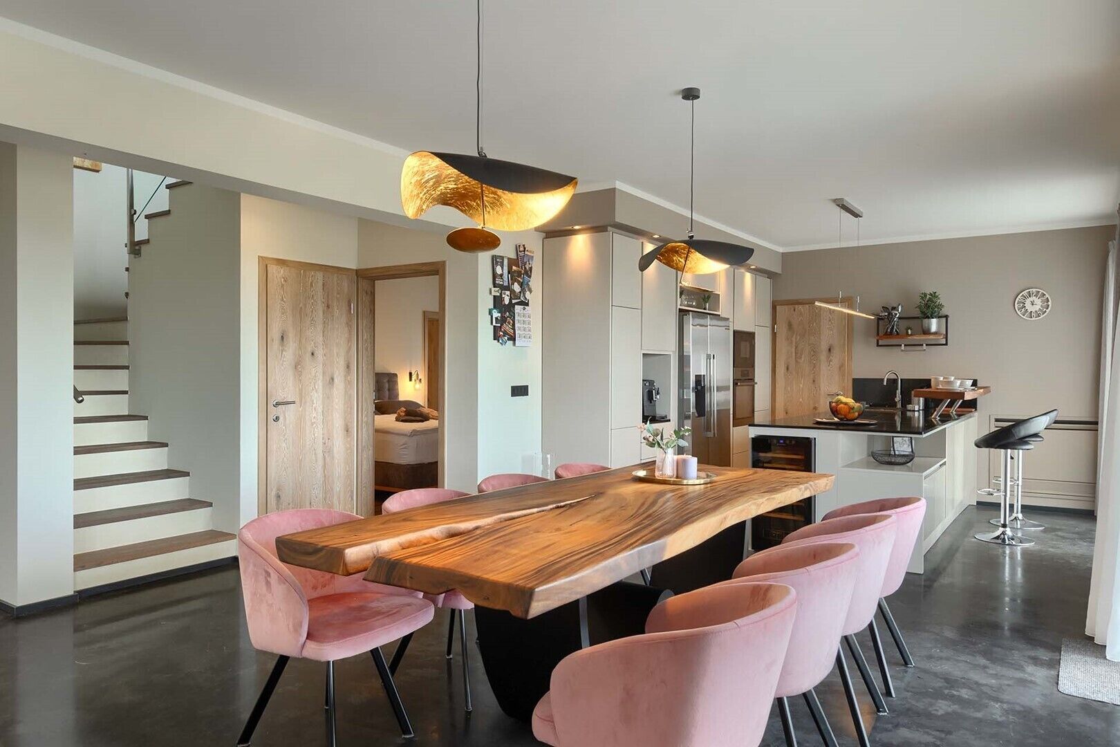 Una cocina moderna con una isla central, electrodomésticos de acero inoxidable y una zona de comedor con mesa de madera y sillas rosas.