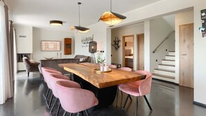 Uma área de jantar moderna com mesa de madeira e cadeiras cor-de-rosa, lareira e escadas que levam a outro andar.