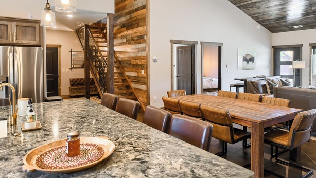 A spacious kitchen with a large island, stainless steel appliances, and a wooden staircase.
