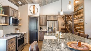 A modern kitchen with a granite island, stainless steel appliances, and a wooden accent wall.