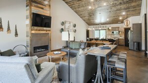 A spacious living area with a fireplace, a dining table, and a kitchen in the background.