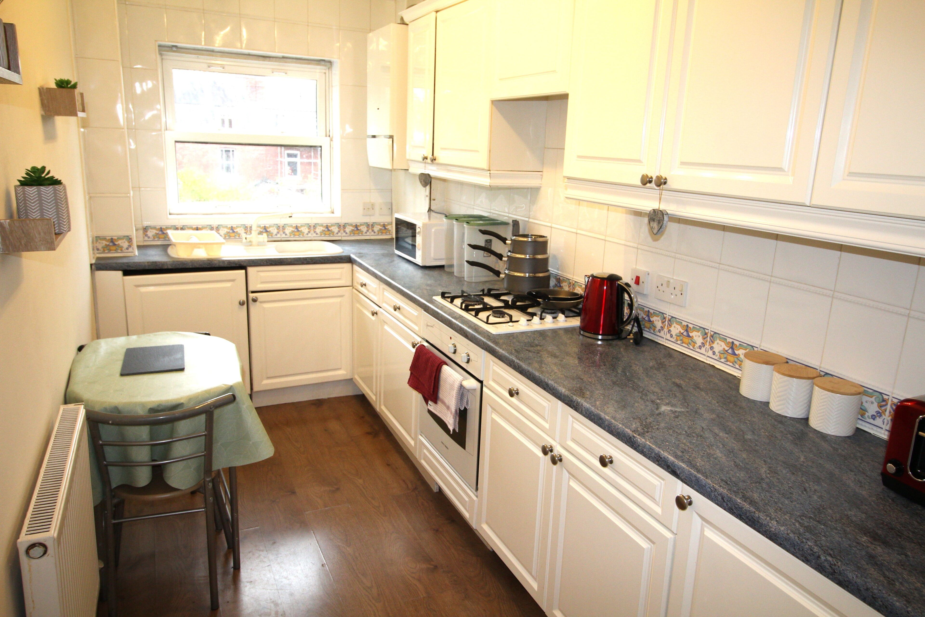 A kitchen with white cabinets, a stove, a microwave, and a window.