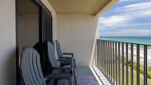 A balcony with chairs, a view of the beach, and a clear sky.