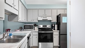 A modern kitchen with white cabinets, a stainless steel sink, a microwave, a stove, and a refrigerator.