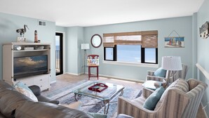 A living room with a TV, comfortable seating, a window with a view, and a beach-themed artwork.