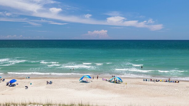 A beach with clear skies, calm waters, and beachgoers.
