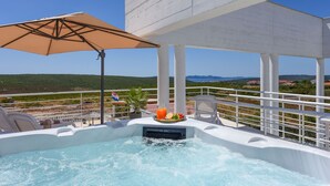 Ein Whirlpool mit Blick auf die Landschaft, ein Tisch mit Obst und Getränken und ein Strand im Hintergrund.